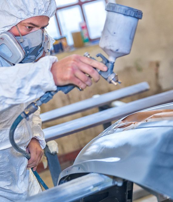Mullinax Body Shop | man wearing white safety gear and a mask while painting an automobile in a body shop